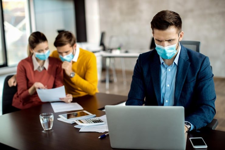 insurance-agent-wit-face-mask-working-laptop-while-his-clients-are-reading-paperwork-background_637285-10908